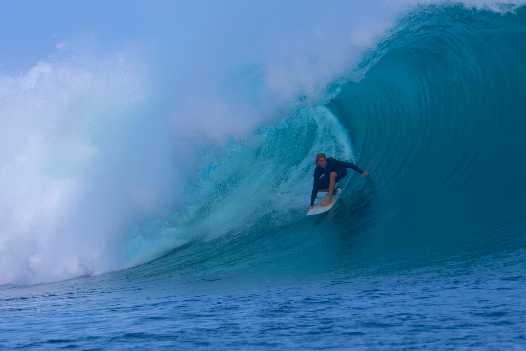 A surfer crouches deep inside a breaking barrel, one hand trailing the wall as the lip throws over him.